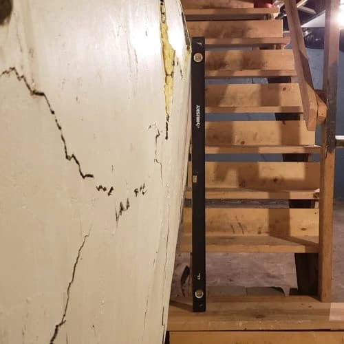 Bowing basement wall with visible cracks and a level tool measuring deflection